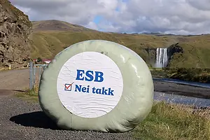 A ROUND, PLASTIC-WRAPPED HAY BALE SPORTS A LABEL WITH A SLOGAN ON IT, BESDIE A ROAD IN ROLLING HILLS