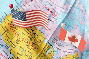 A GLOBE MAP SHOWING THE US AND CANADA, WITH FLAGS OF EACH COUNTRY ON PINS STUCK IN TO EACH COUNTRY