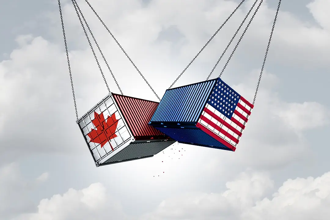 A shipping container bearing the Canadian flag swings in the air against a container bearing the American flag