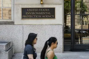 TWO PEOPLE WALK PAST A BRASS SIGN AFFIXED TO A BUILDING