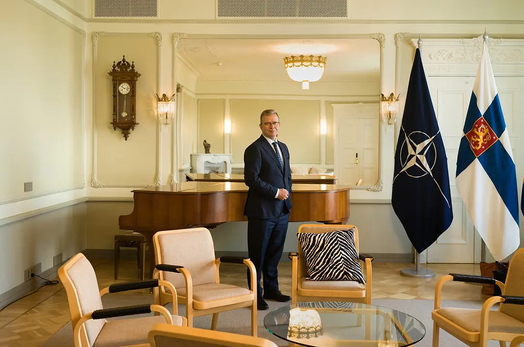 A MAN IN A SUIT AND TIE STANDS IN A PALE, PANELED ROOM