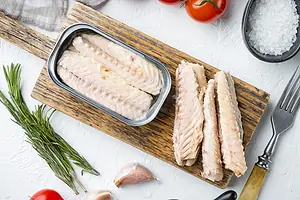 Canned Mackerel Fillets in Tin, on wooden cutting board, on white background with herbs and ingredients