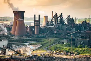 SMOKE AND STEAM EMERGE FROM GIANT CHIMNEYS IN A STEEL WORKS PLANT
