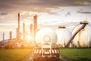 A fuel truck driving toward a refinery at sunset