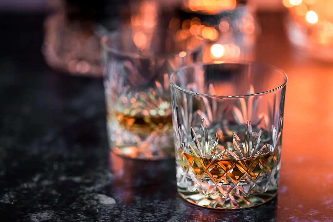 Crystal glasses of whisky sit on a weathered surface