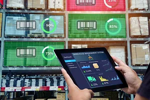 A person holding a tablet with charts and graphs, standing in front of a warehouse shelf