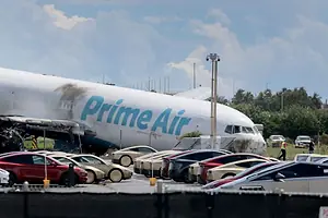 AN AIRPLANE BEARING THE PRIME AIR LOGO SITS CRASHED BEHIND A PARKING LOT