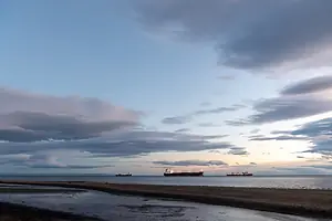 A view from a beach shore of three container vessels at sea in the distance