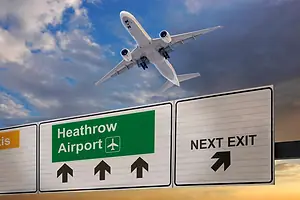 A road sign indicating the direction of Heathrow airport and a plane that just took off