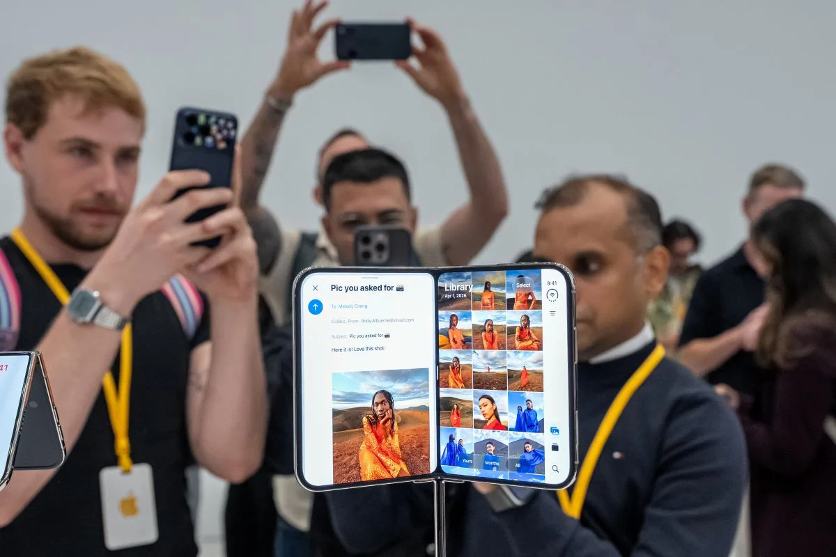 A CROWD OF MEN WEARING LANYARDS CLUSTER AROUND A IPHONE DUO, TAKING PICTURES WITH THEIR SMART PHONES