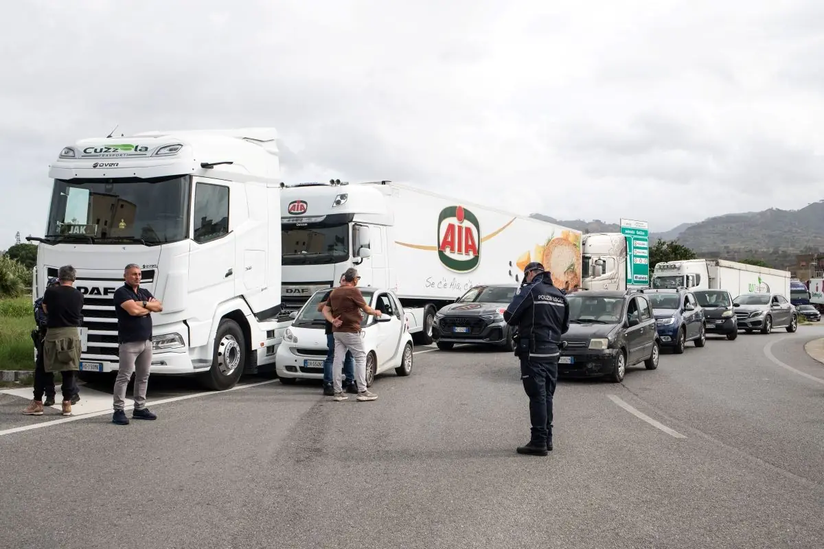 police and truckers stand with their arms folded in front of a truck that's blocking a long line of cars