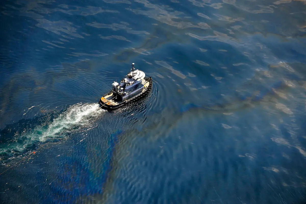 An overhead view of a tugboat moving through oil-contaminated waters