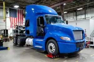 A BLUE TRUCK TRACTOR SITS ON A FACTORY FLOOR WITH AN AMERICAN FLAG VISIBLE BEHIND